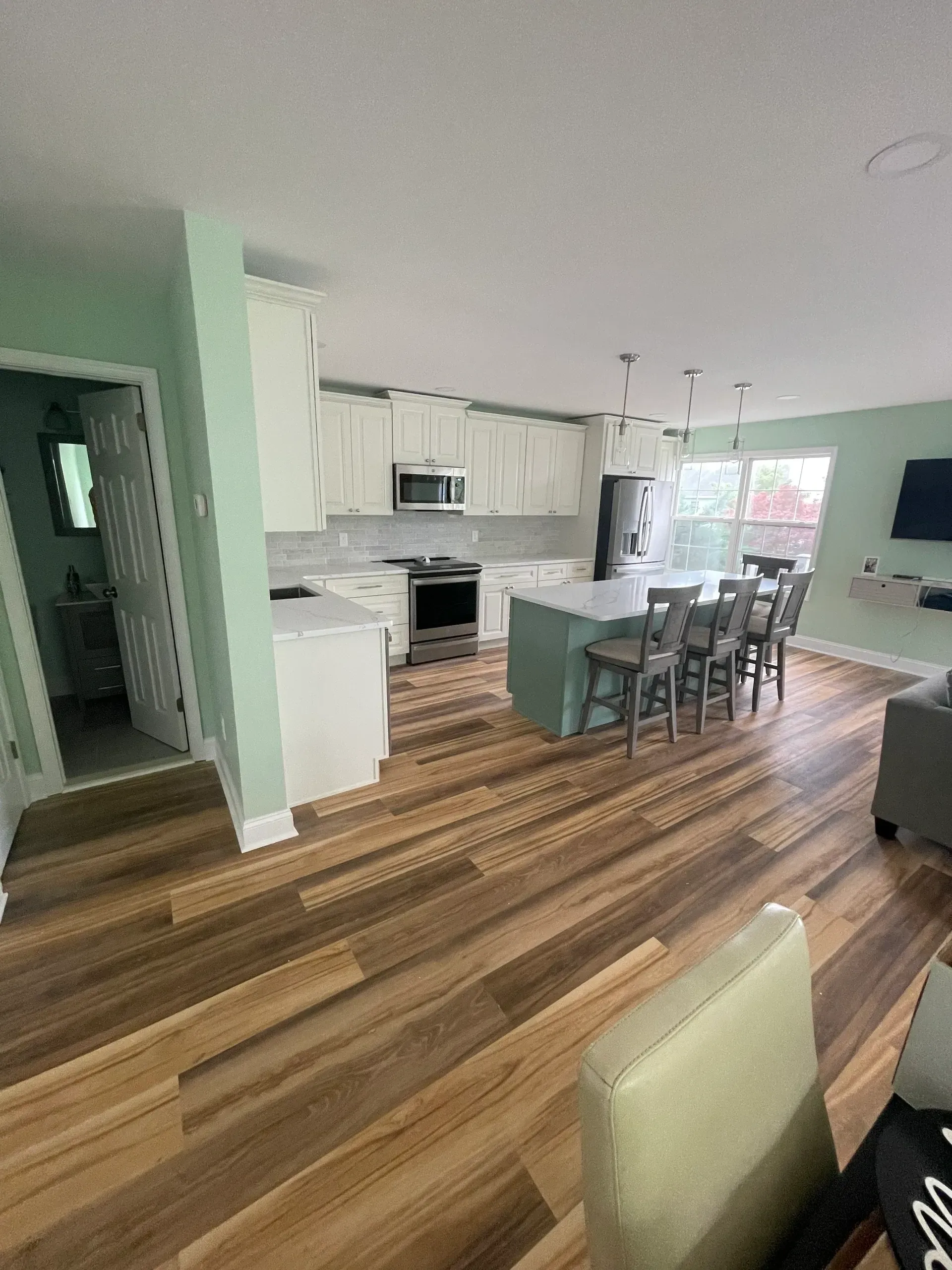 Open-concept kitchen with white cabinets, aqua island, light wood floors, and mint green walls.