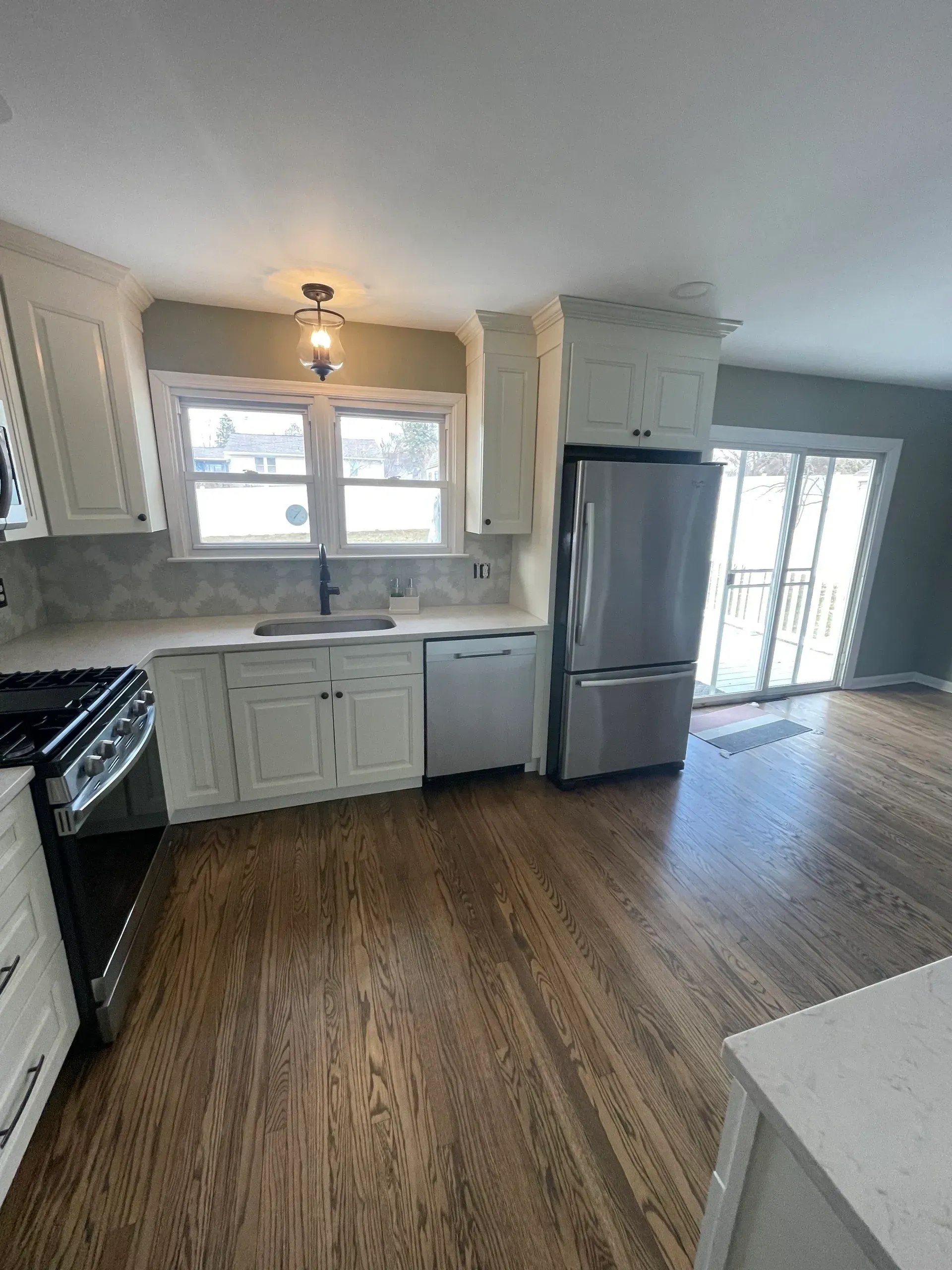 White kitchen with stainless steel appliances, dark wood floors, and a view of a sliding glass door.