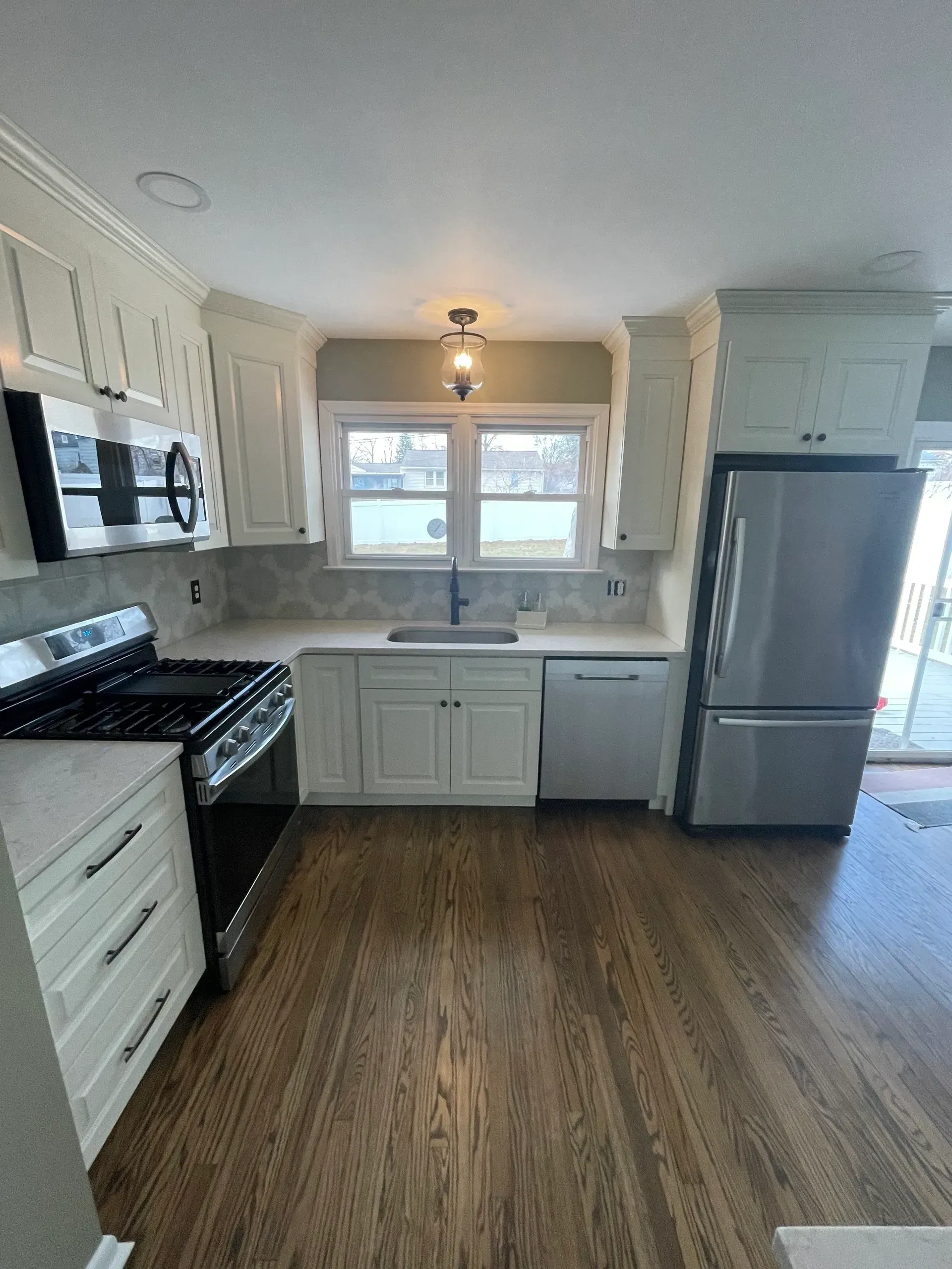 Modern kitchen with white cabinets, stainless steel appliances, and wood flooring.