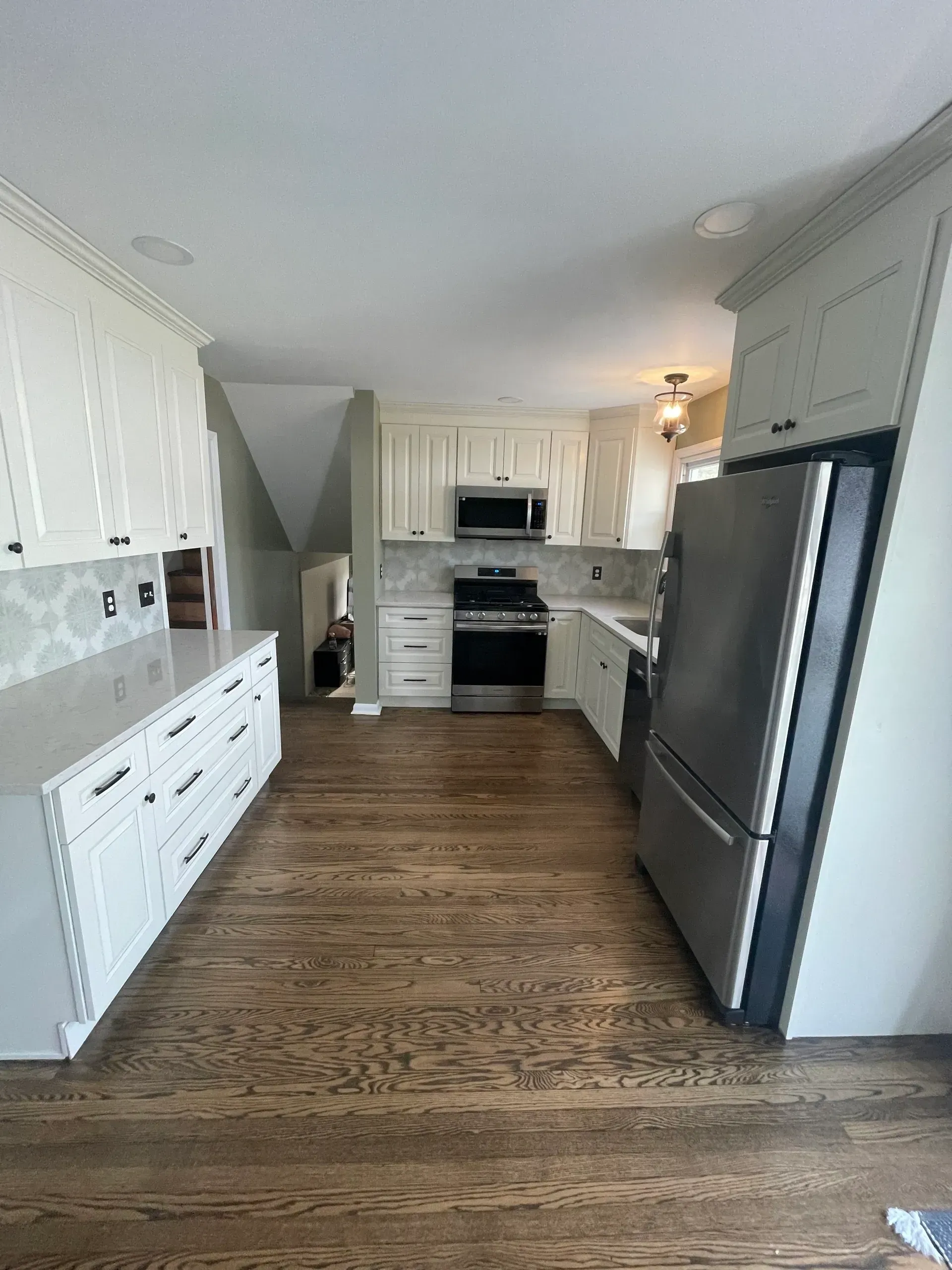 White kitchen with wood floor, stainless steel appliances, and white cabinets.