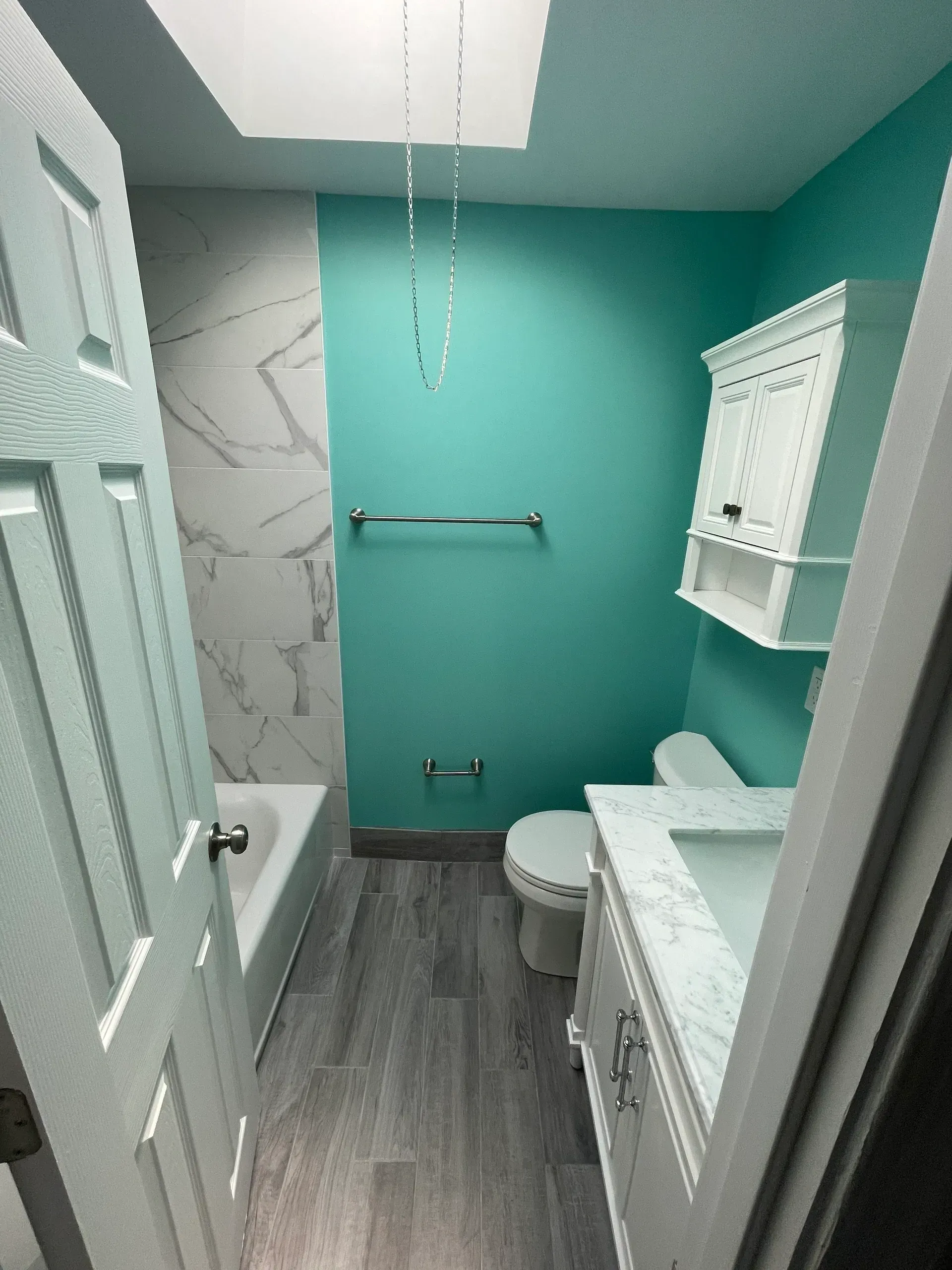 Bathroom with teal wall, marble-look tile, white vanity, toilet, and cabinet.