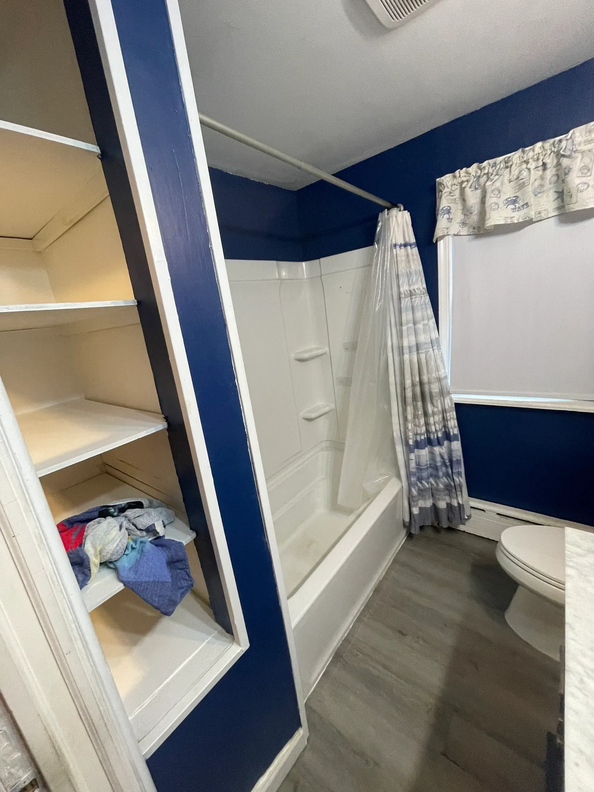 Bathroom with blue walls, white tub, and built-in shelving. Gray floor, shower curtain.