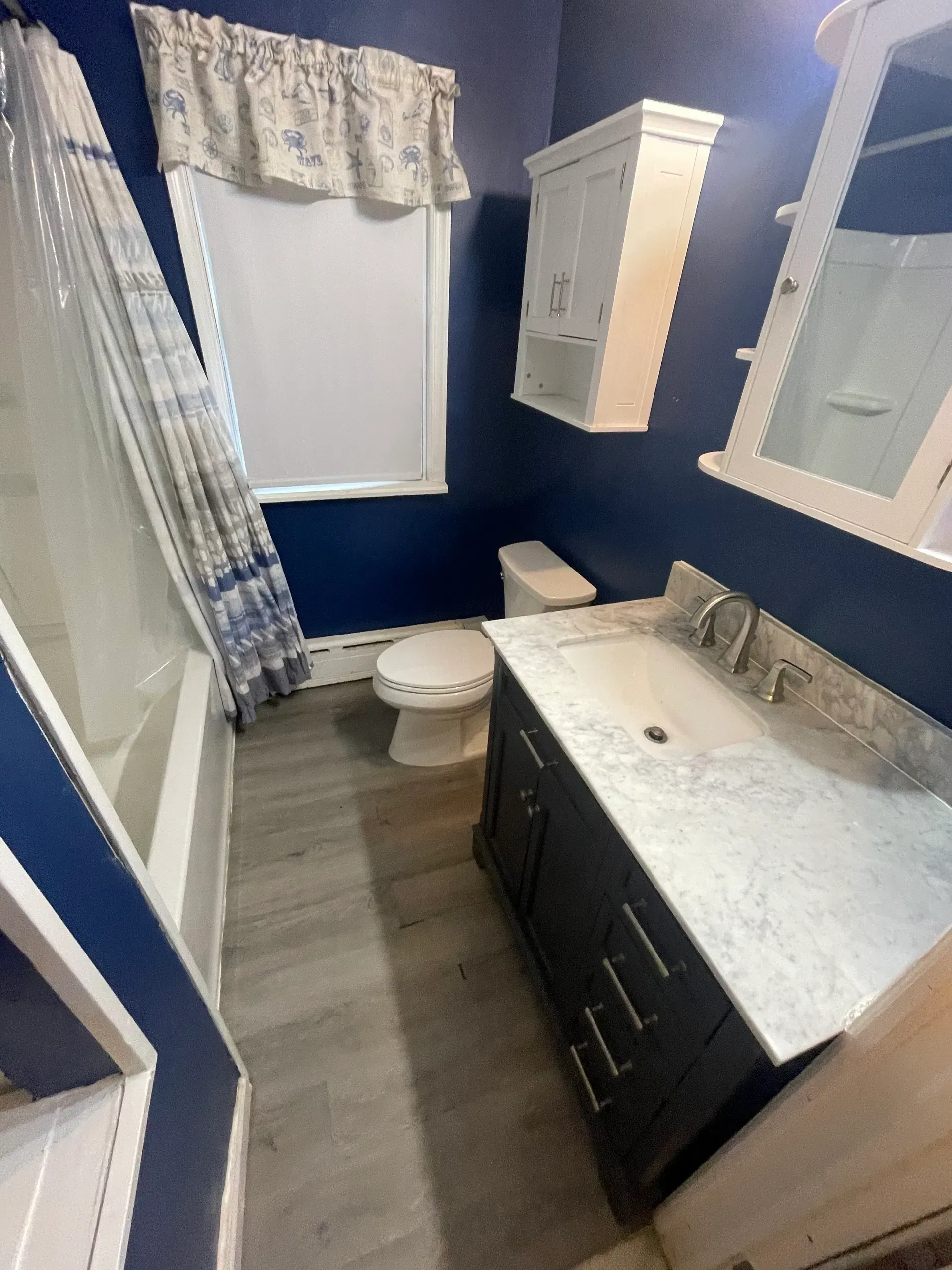 Bathroom with blue walls, white trim, grey floor, toilet, vanity, and shower.