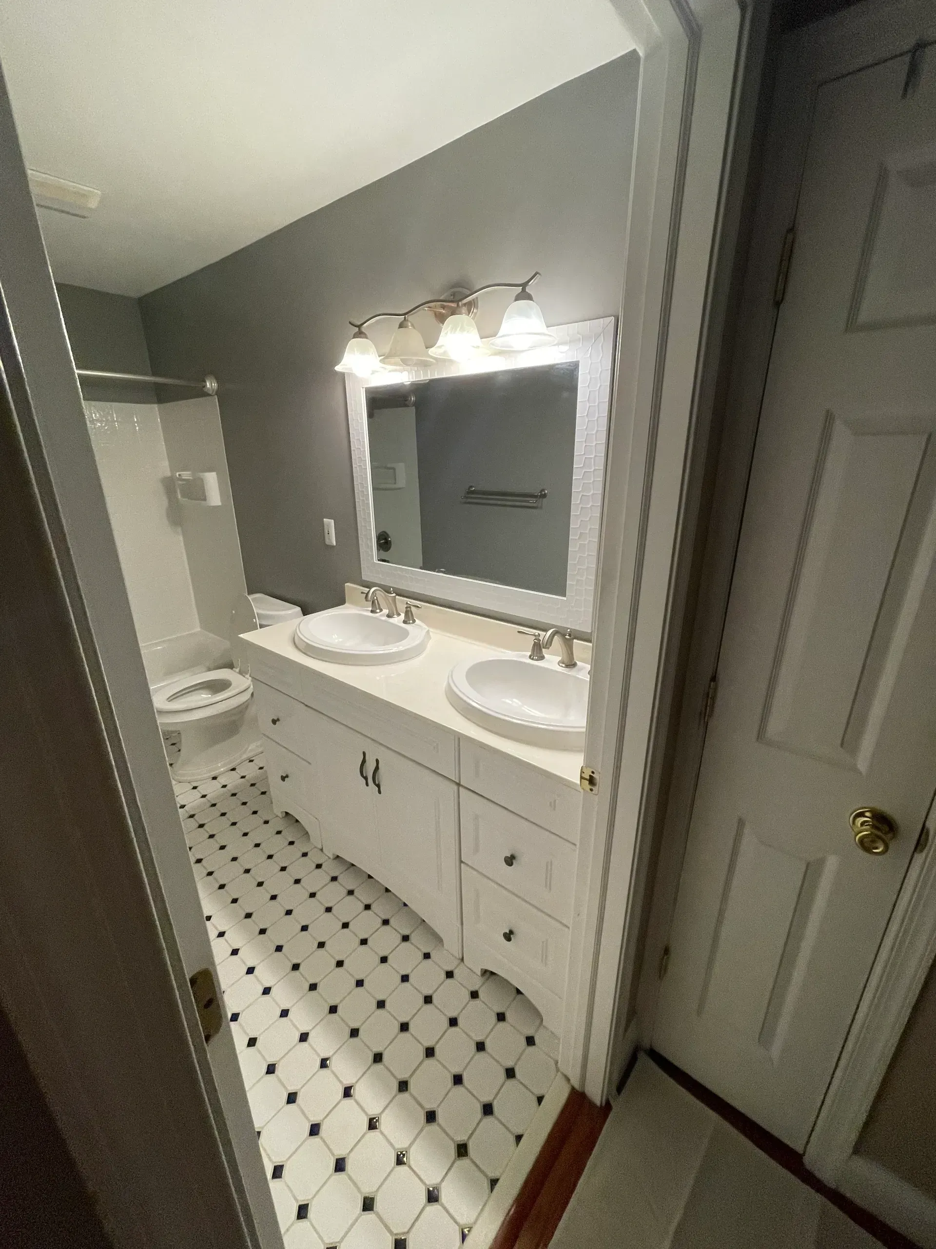 Bathroom with white double vanity, white and black tile floor, gray walls.