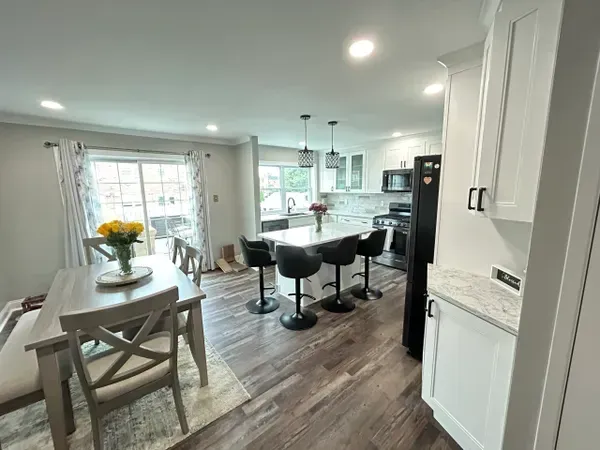 Modern kitchen with island, dining area, white cabinets, and dark appliances.