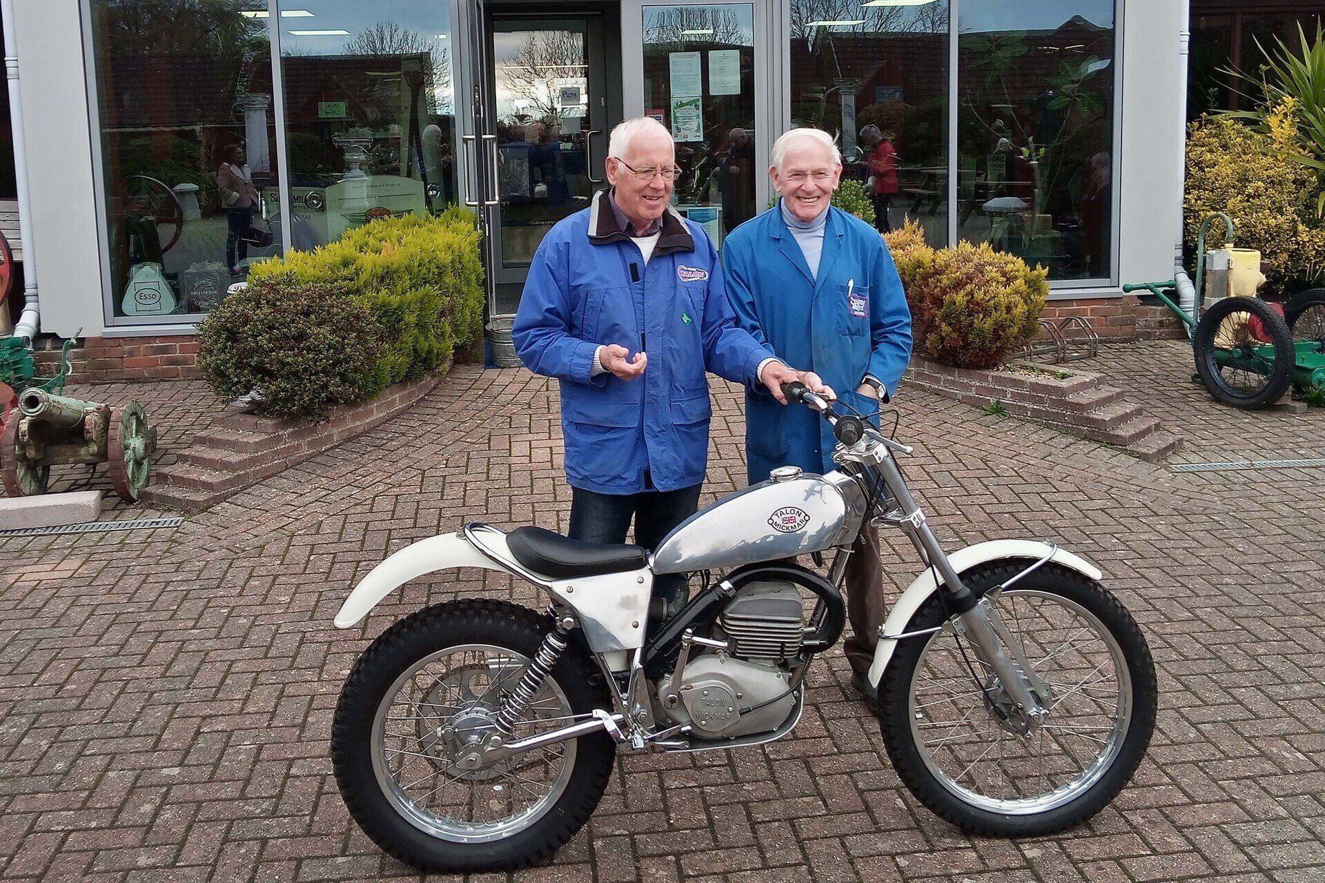 Two men are standing next to a motorcycle in front of a building