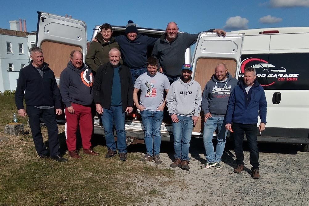 A group of men standing in front of a white van with the word garage on the side