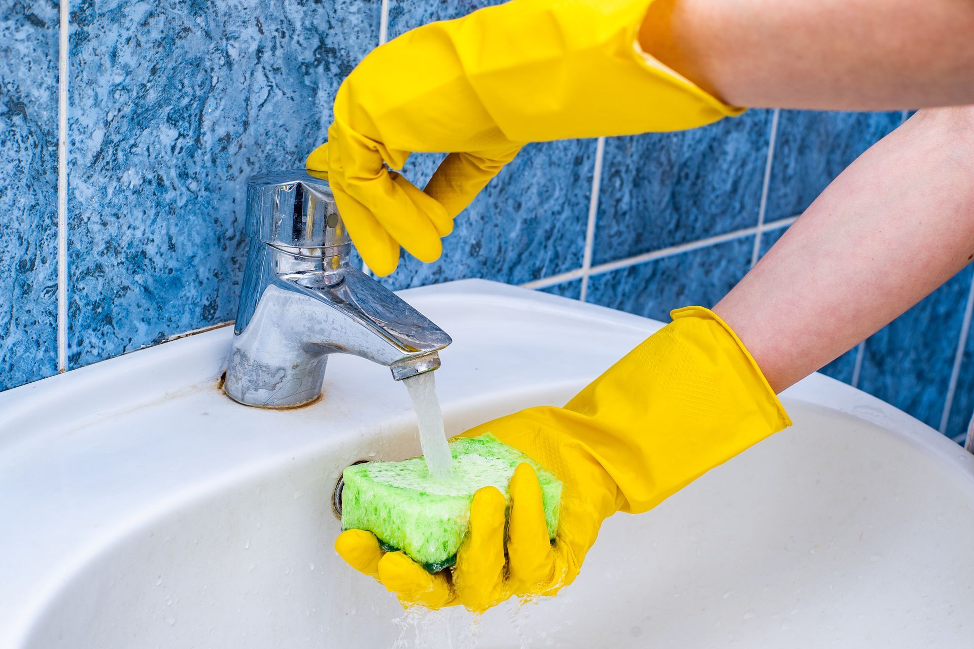 A person wearing yellow gloves is washing a sink with a sponge.