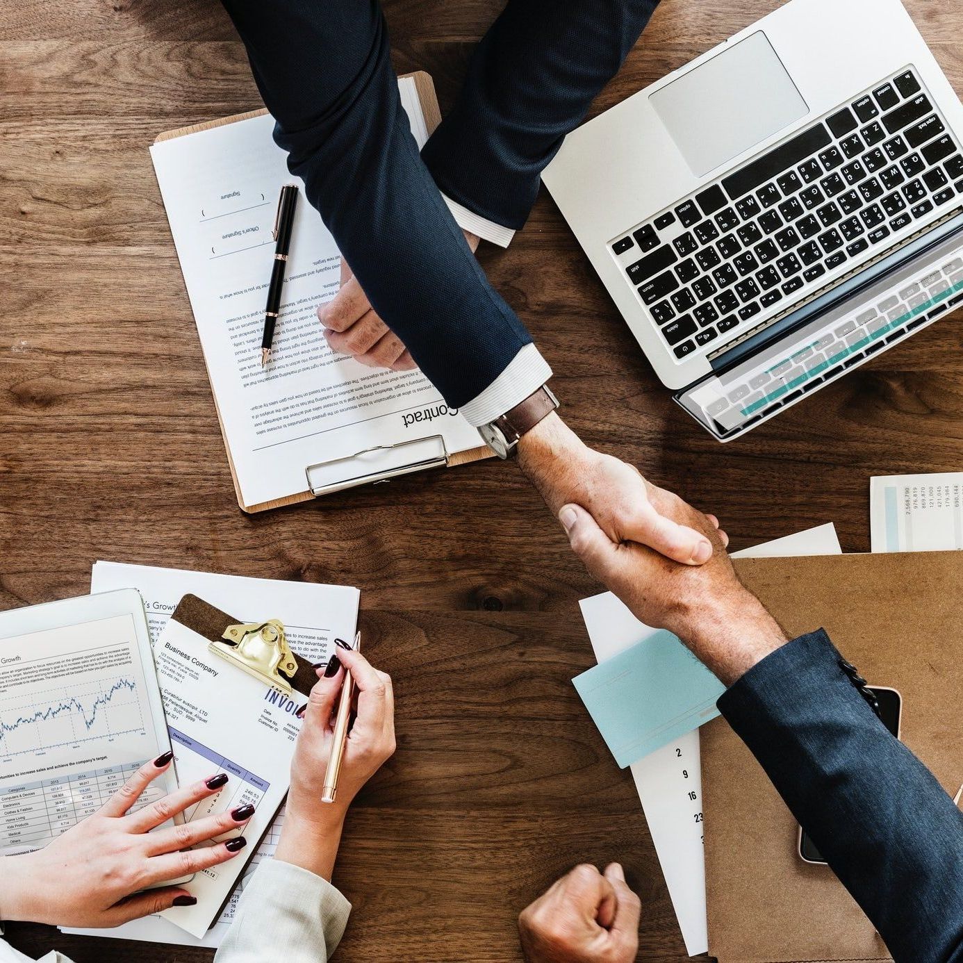 A man and a woman are shaking hands over a wooden table.