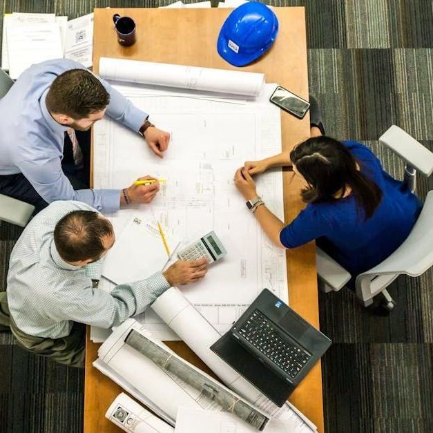 A group of people are sitting around a table looking at blueprints