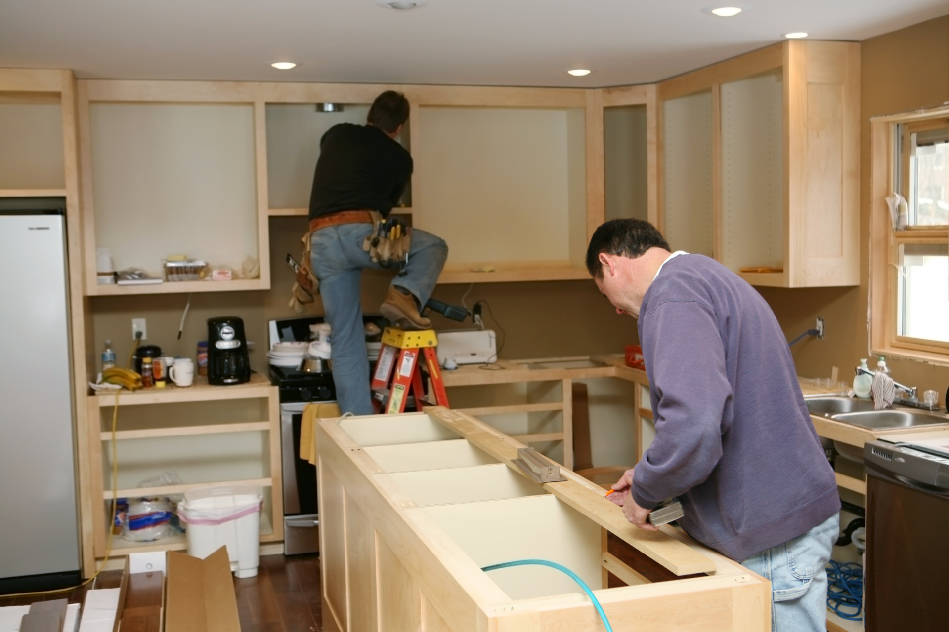 Two people installing kitchen cabinets in a bright, unfinished kitchen