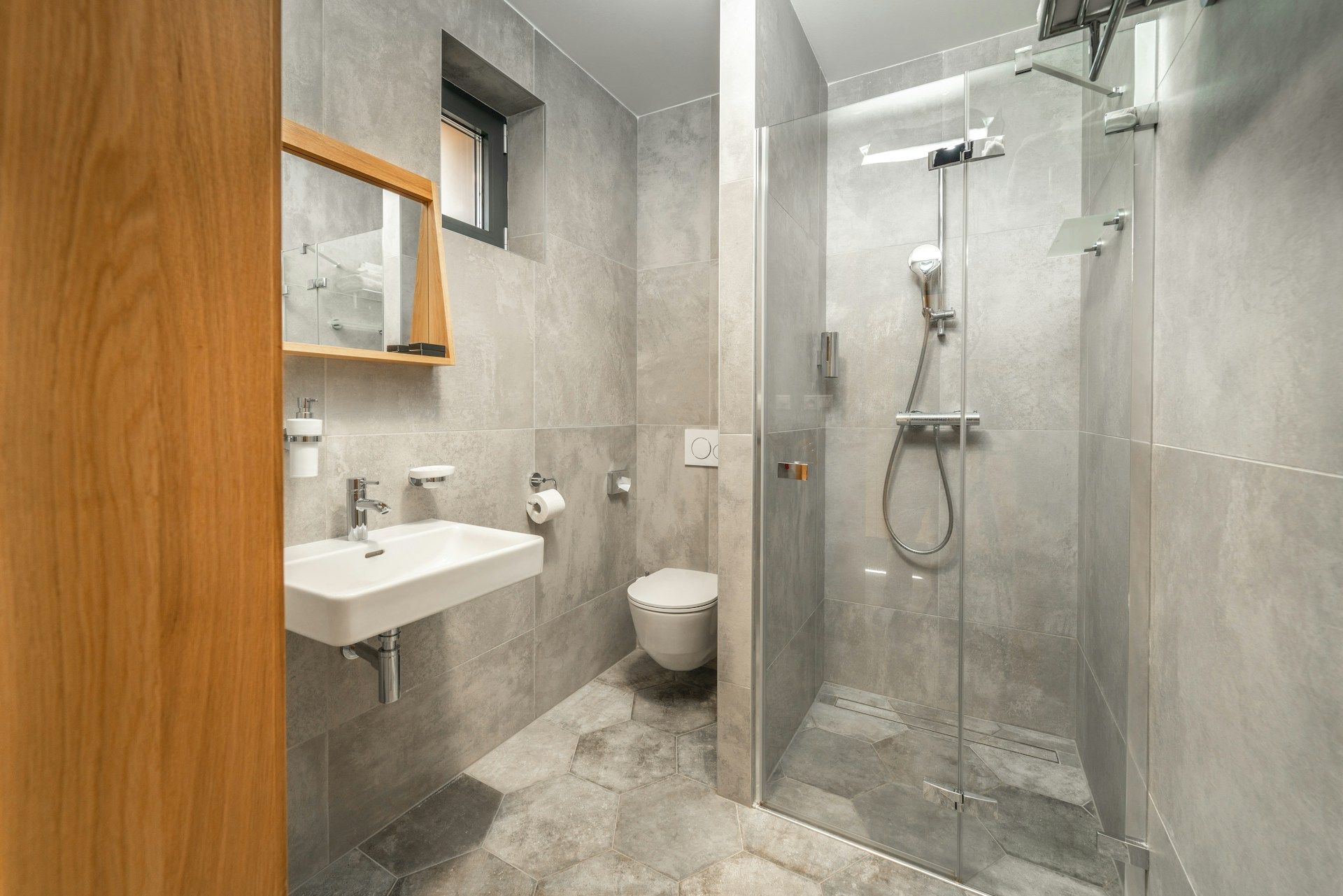 Modern bathroom with gray and white tile, glass shower, white tub, and toilet.