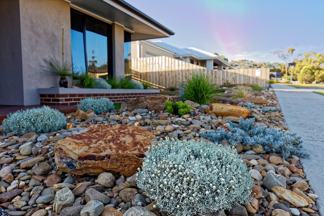 A rock garden in front of a house with a rainbow in the background.
