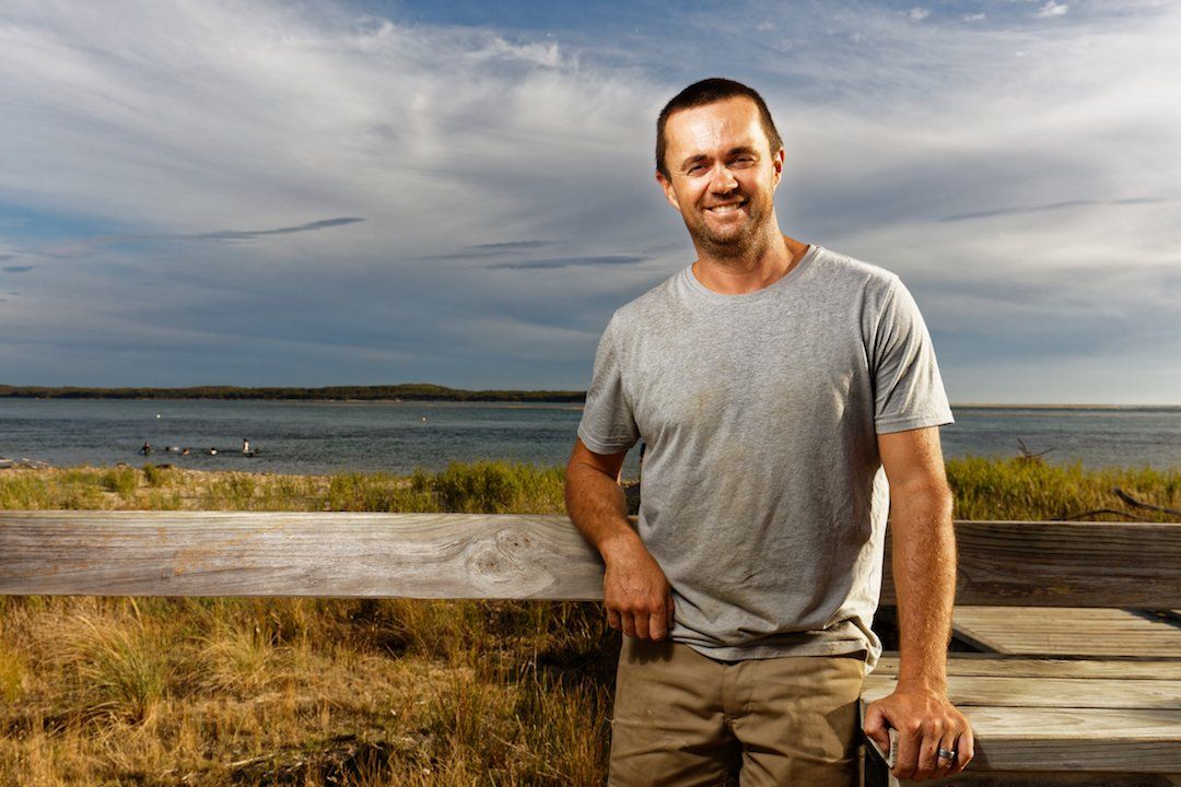 A man is leaning on a wooden fence next to a body of water.