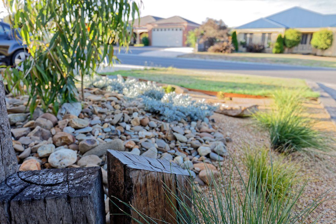 A rock garden in front of a house with a car parked in the driveway.