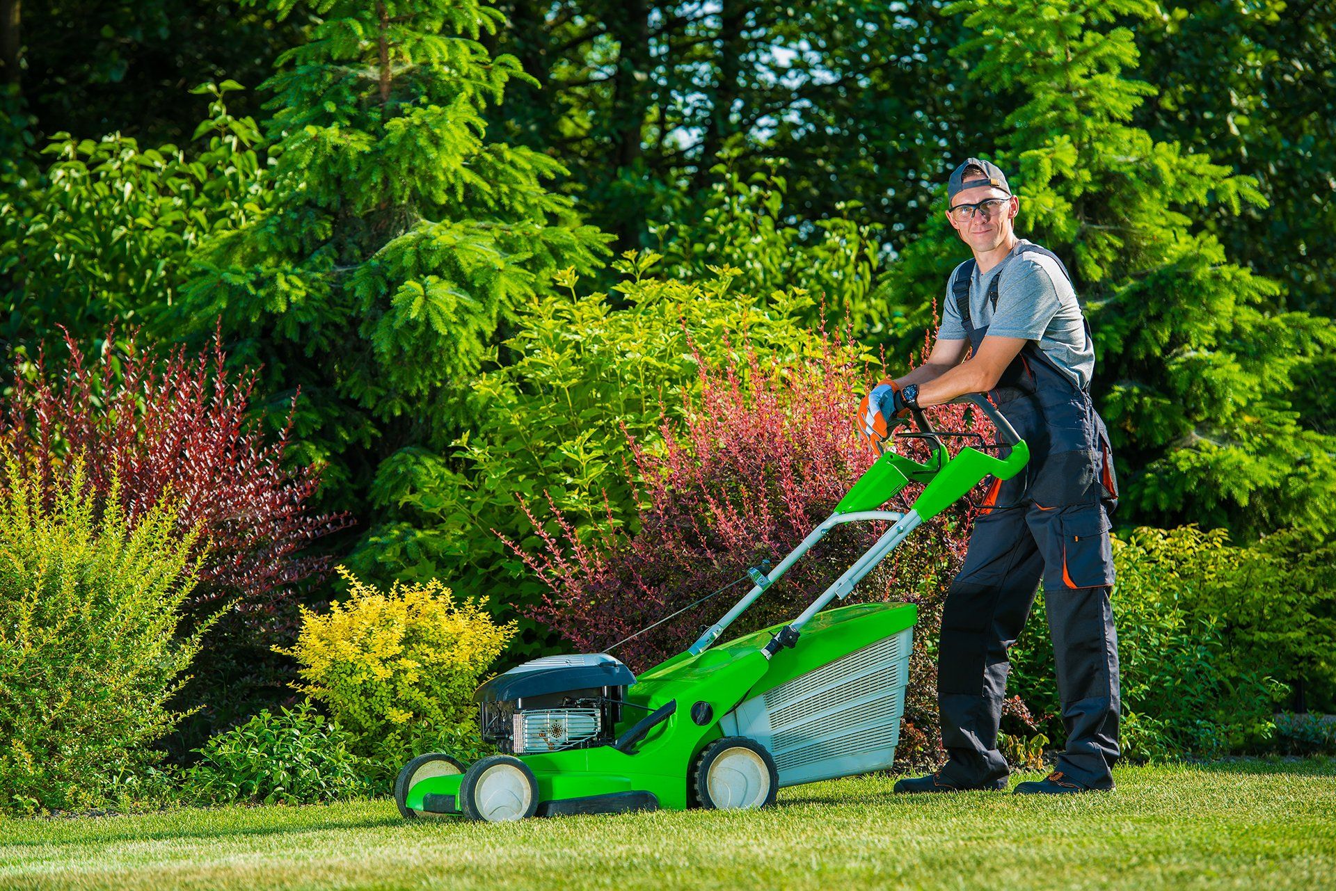 A man is cutting the grass with a green lawn mower.