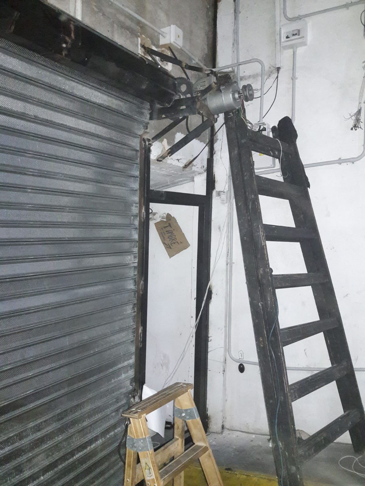 Una escalera de madera está apoyada contra una persiana metálica.