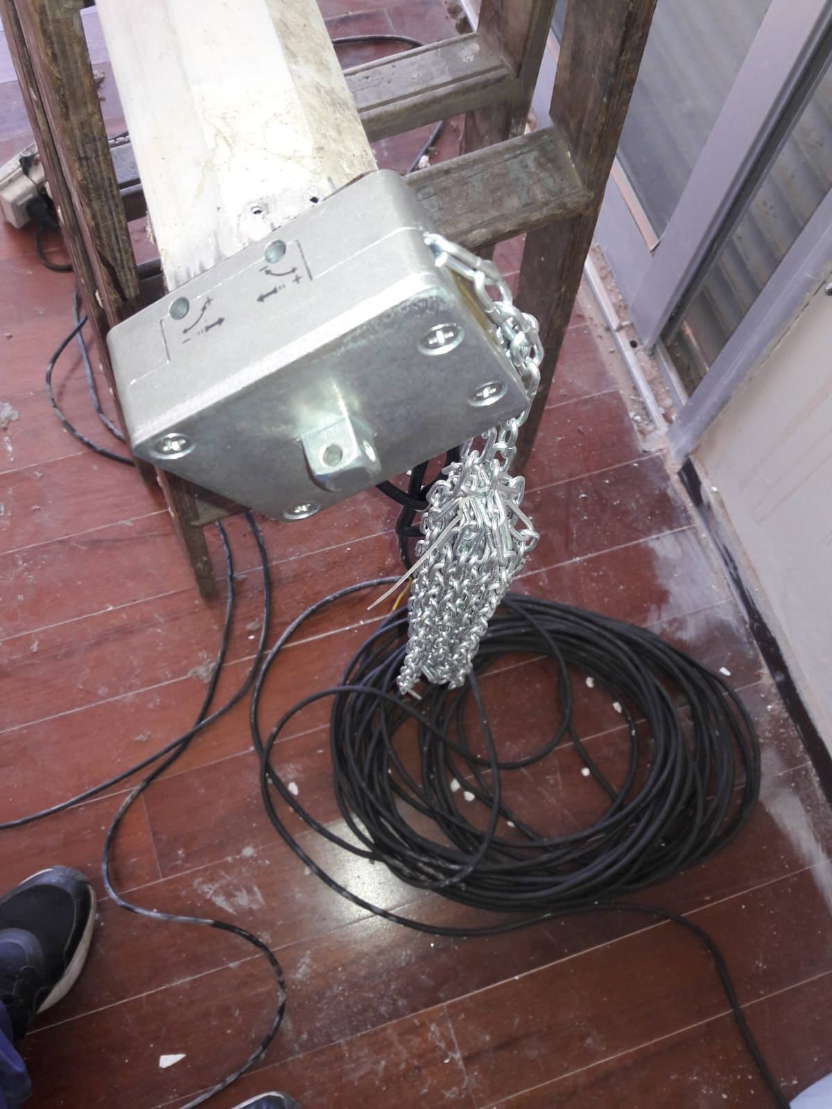 Una cadena cuelga de una caja de metal en un piso de madera al lado de una escalera.
