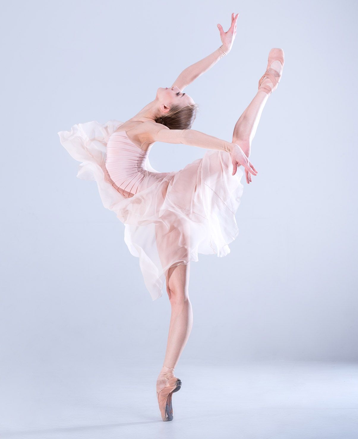 A ballerina in a pink dress and pointe shoes is dancing on a white background.