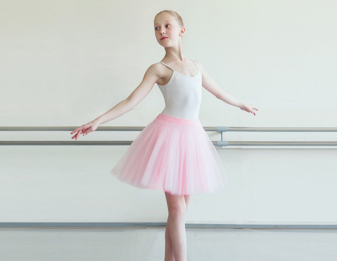 A young ballerina in a pink tutu is standing in a dance studio.