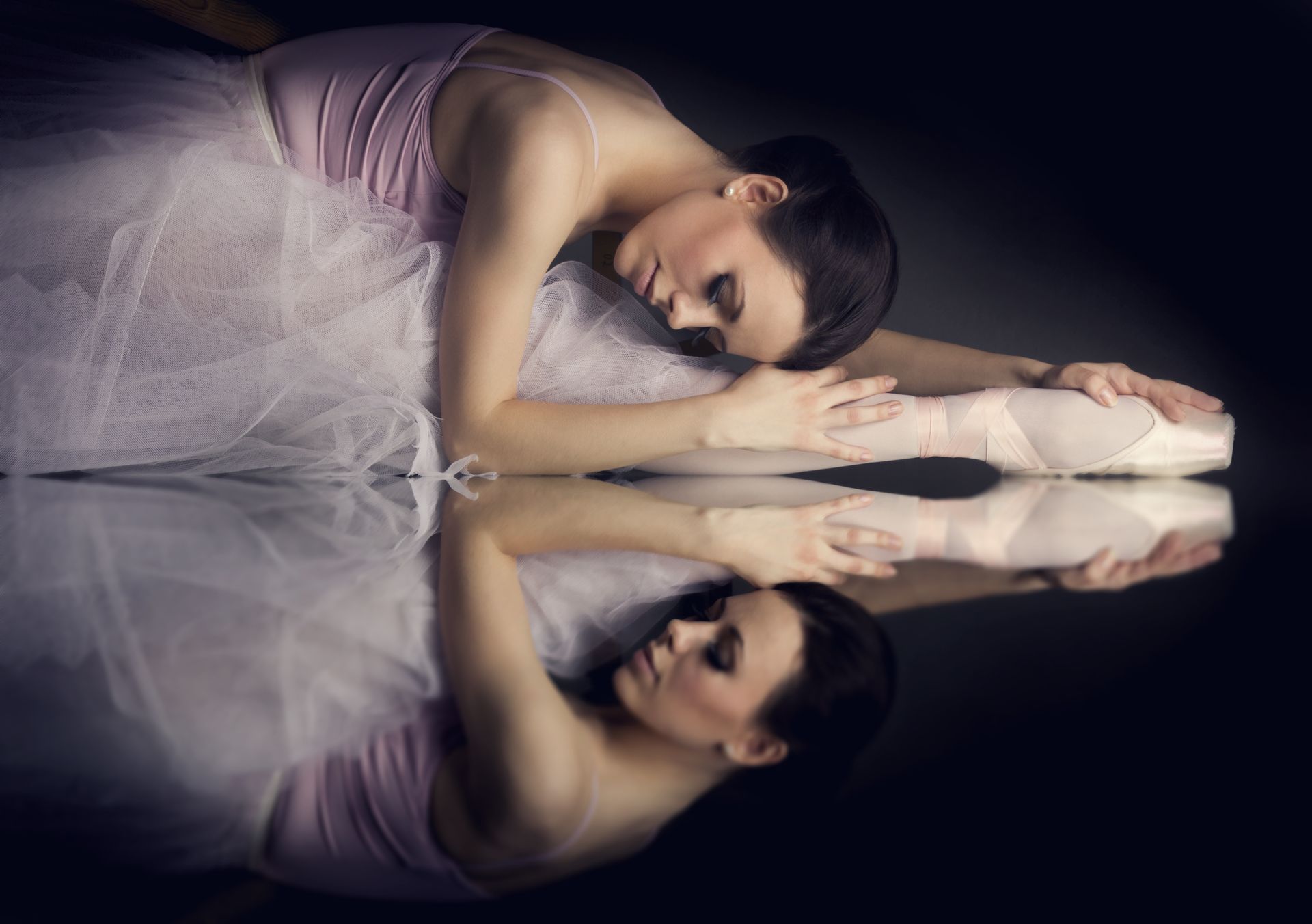 A ballerina is laying down and her reflection is in the mirror