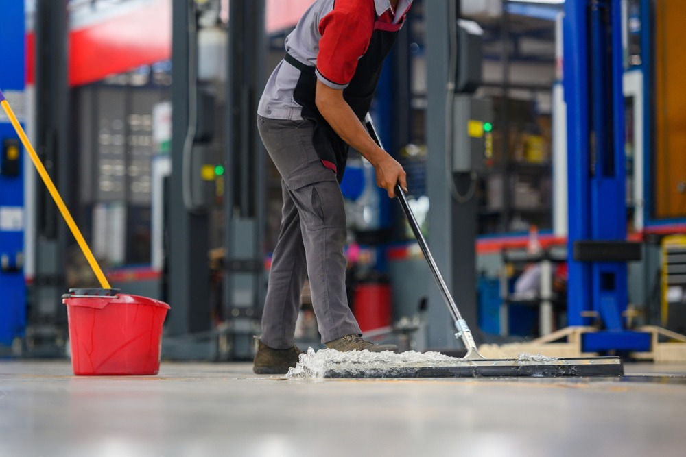 A man is mopping the floor of a garage with a mop.