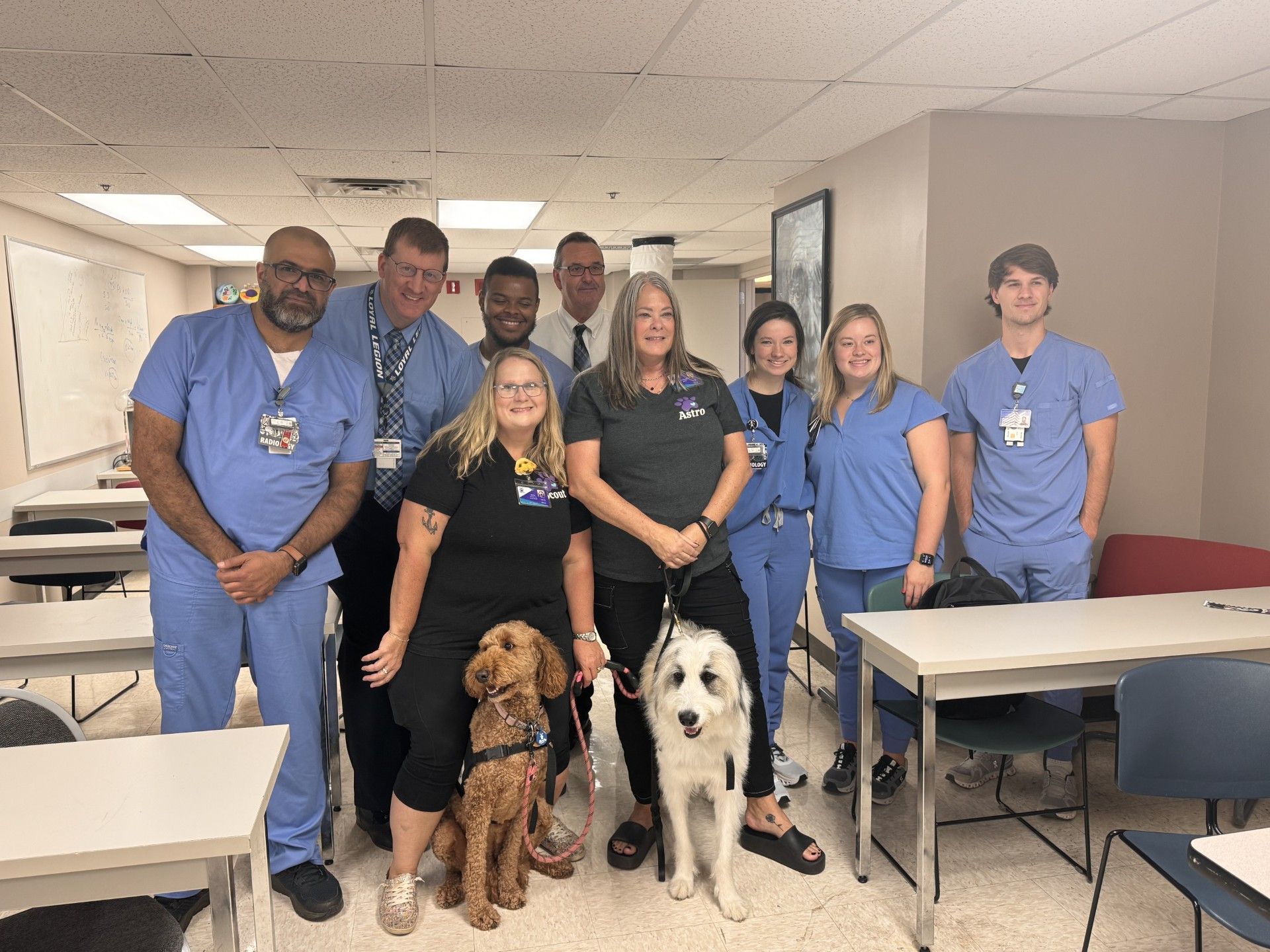 A group of people and a dog are posing for a picture in a classroom.