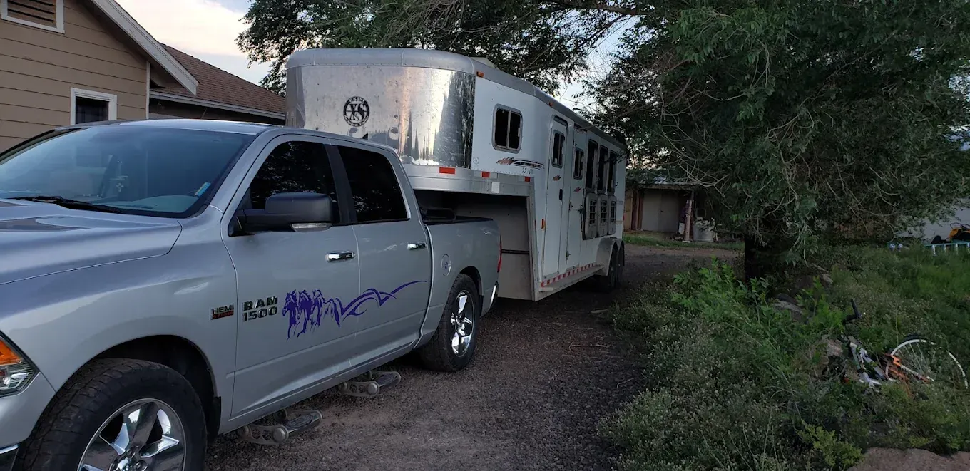 A silver truck with a trailer attached to it is parked in front of a house.