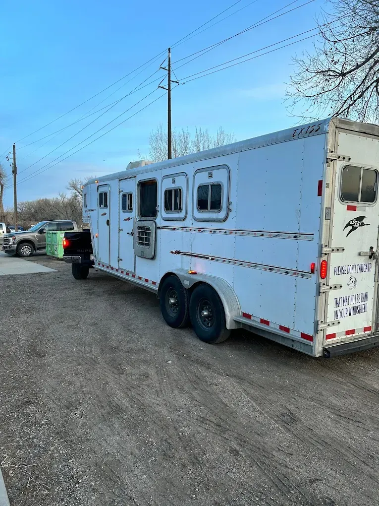 A white horse trailer is parked in a dirt lot next to a truck.