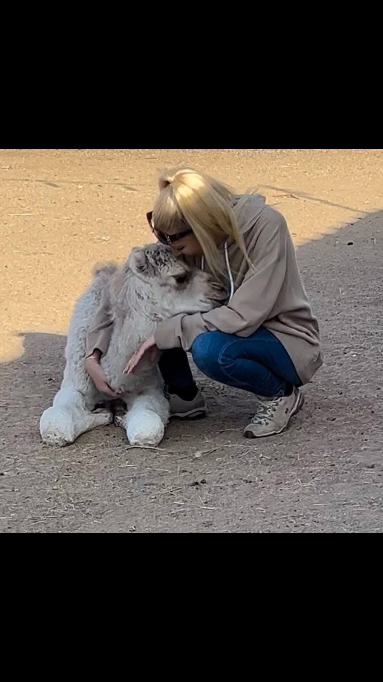 A woman is kneeling down next to a stuffed animal.
