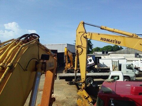 Yellow Komatsu excavator near other vehicles under a bright blue sky.