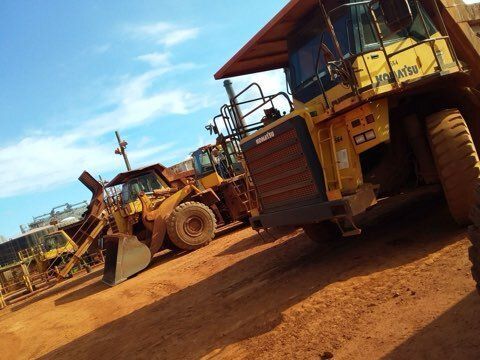 Heavy yellow construction vehicles on a reddish dirt surface under a blue sky.