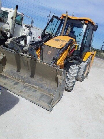 Yellow JCB backhoe loader with a front bucket, parked on concrete.