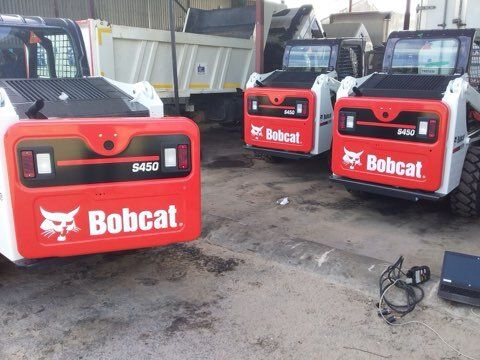 Three Bobcat S450 skid-steer loaders with red and white details are parked in a garage-like setting.
