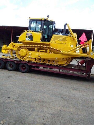 Yellow bulldozer on a red trailer, parked on a gray surface.