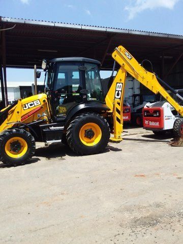 Yellow and black JCB backhoe loader on a concrete surface; a red and white Bobcat is behind it.