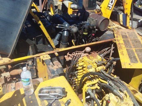 Yellow construction equipment engine compartment open for repair; rusty components, water bottle.