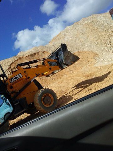 Yellow JCB loader digging into a large sand pile under a blue sky with clouds.