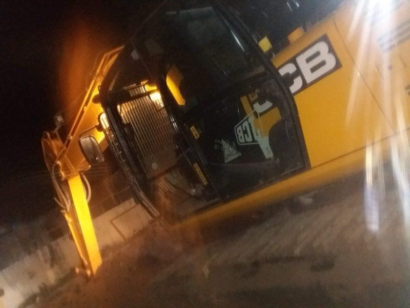 Yellow JCB excavator at night, cab door open, working.