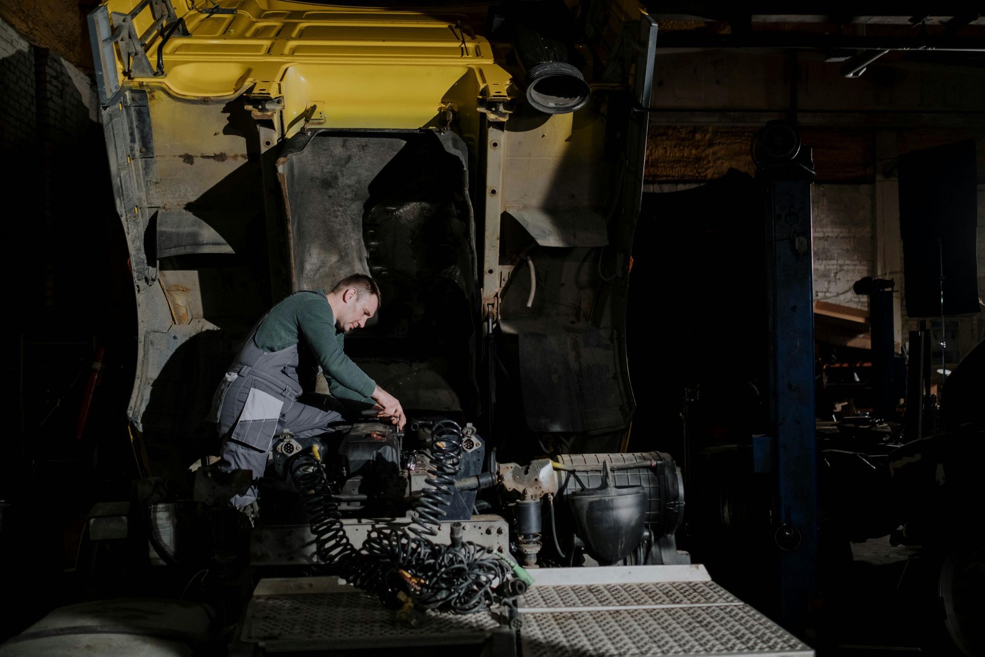 Mechanic working on a large yellow vehicle engine in a dimly lit garage.