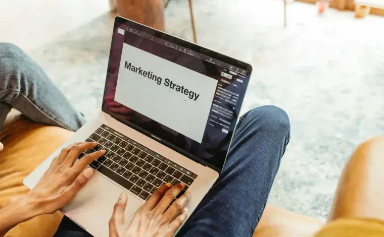 Person using a laptop on a couch with “Marketing Strategy” on the screen