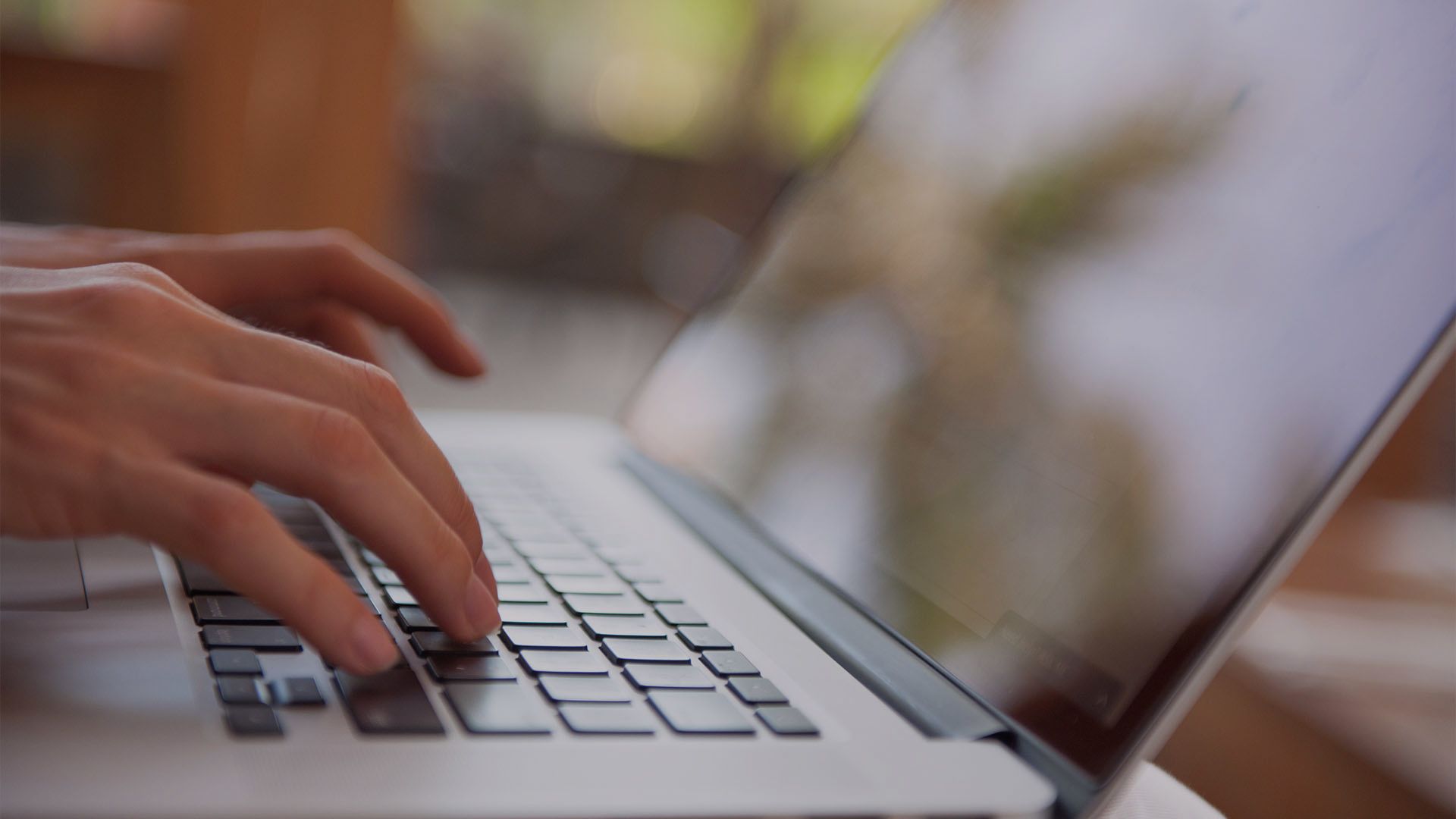 Hands typing on a laptop keyboard beside a blurred screen
