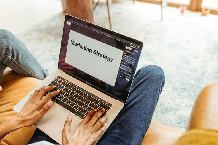 Person using a laptop on a couch with “Marketing Strategy” on the screen