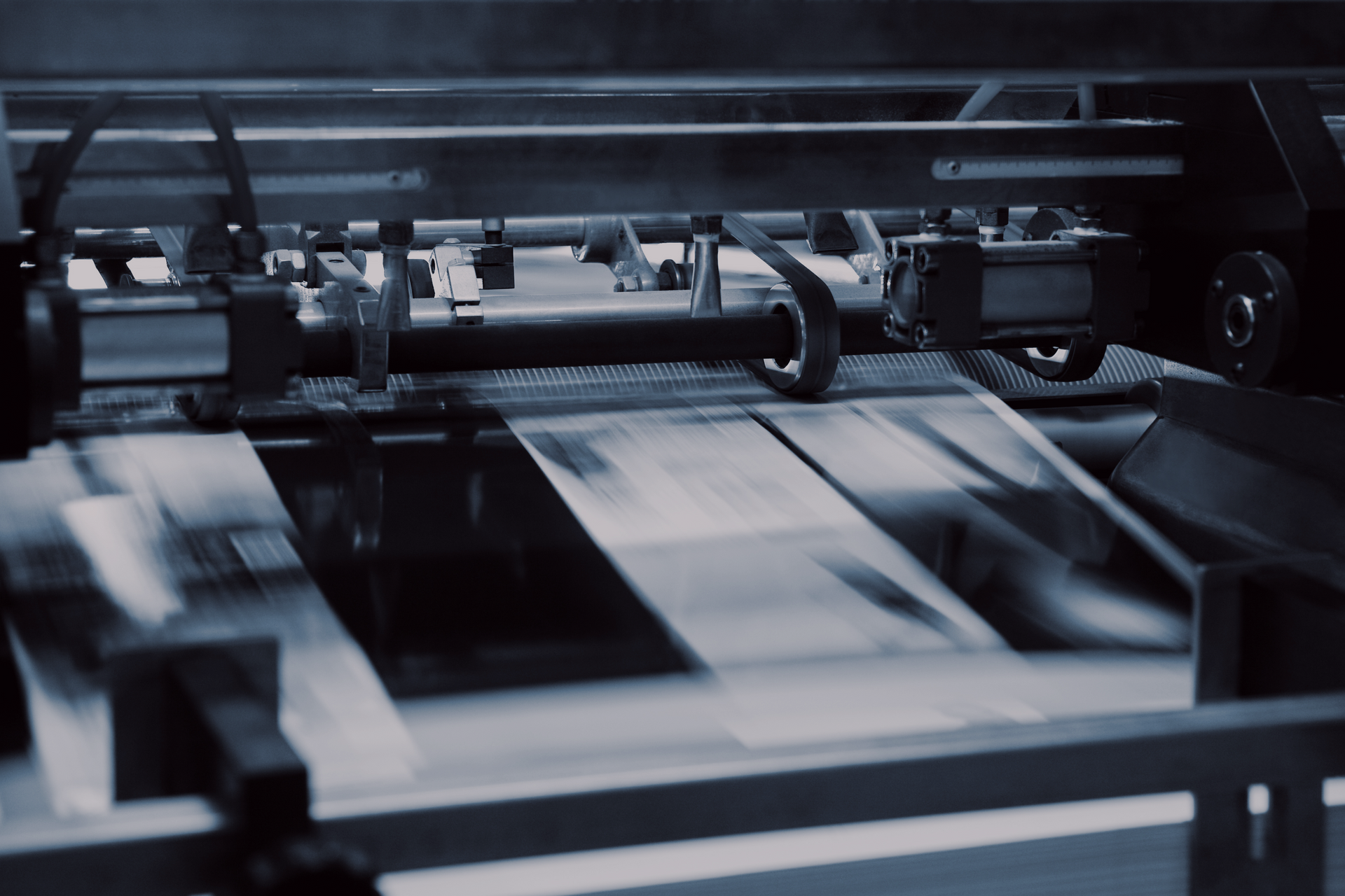 Industrial machine processing sheets in a factory, with moving rollers and blurred paper feed.