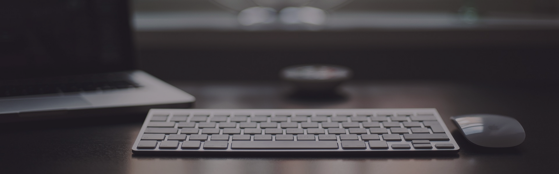 Minimal desktop setup with a keyboard and mouse on a dark desk рядом a laptop screen