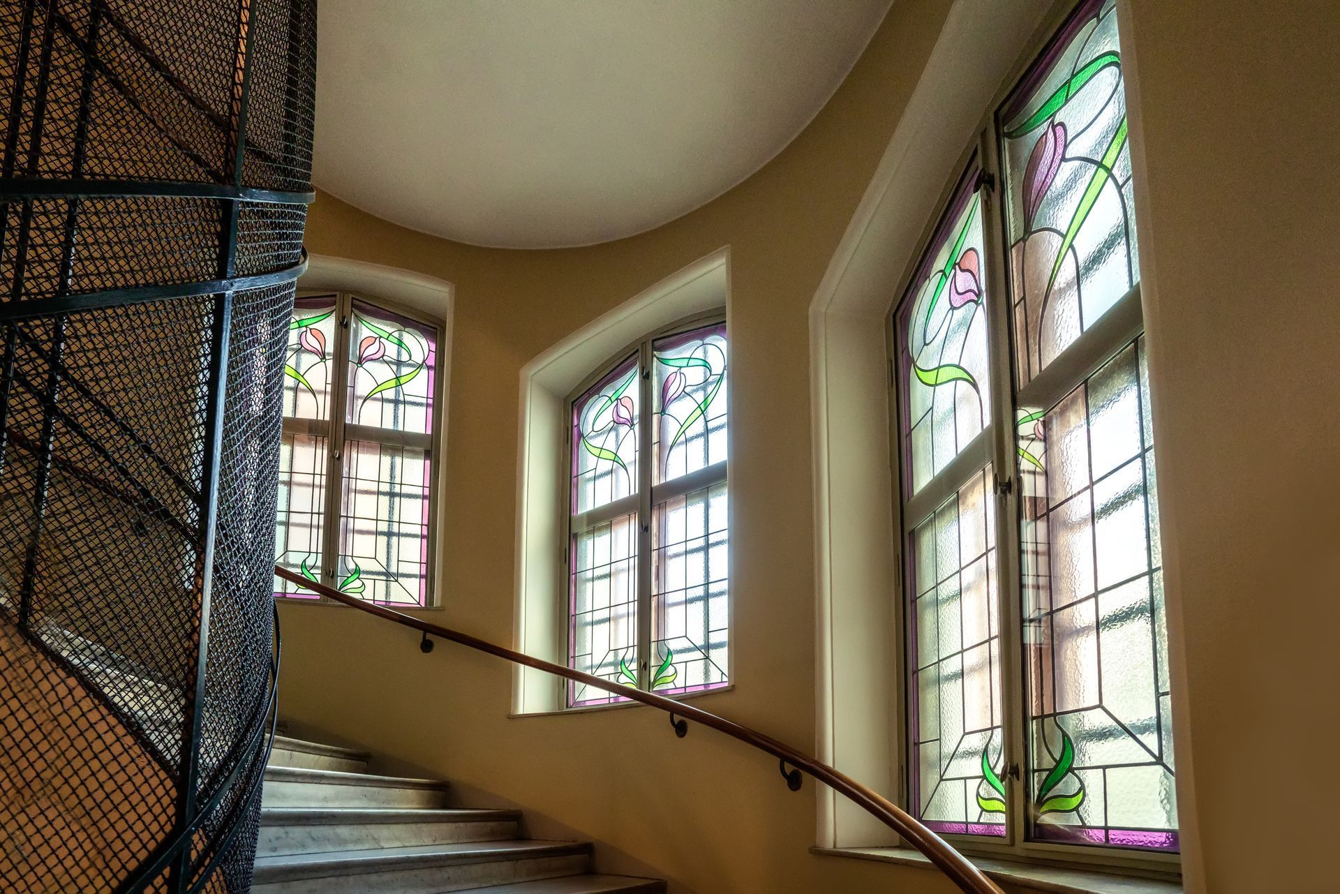 Curved staircase beside stained-glass windows in a softly lit interior hallway