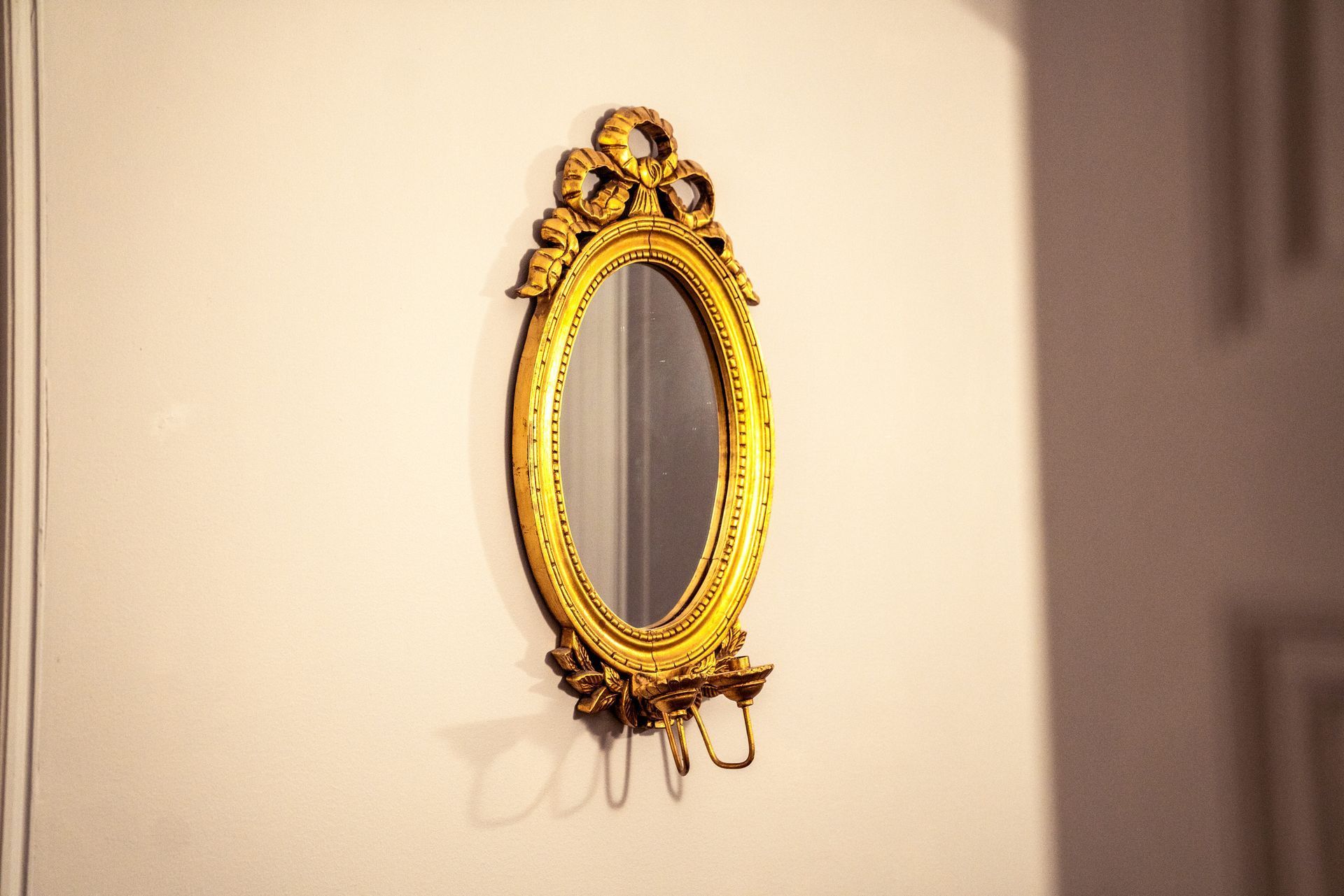 Ornate gold oval mirror hanging on a cream wall, casting a soft shadow