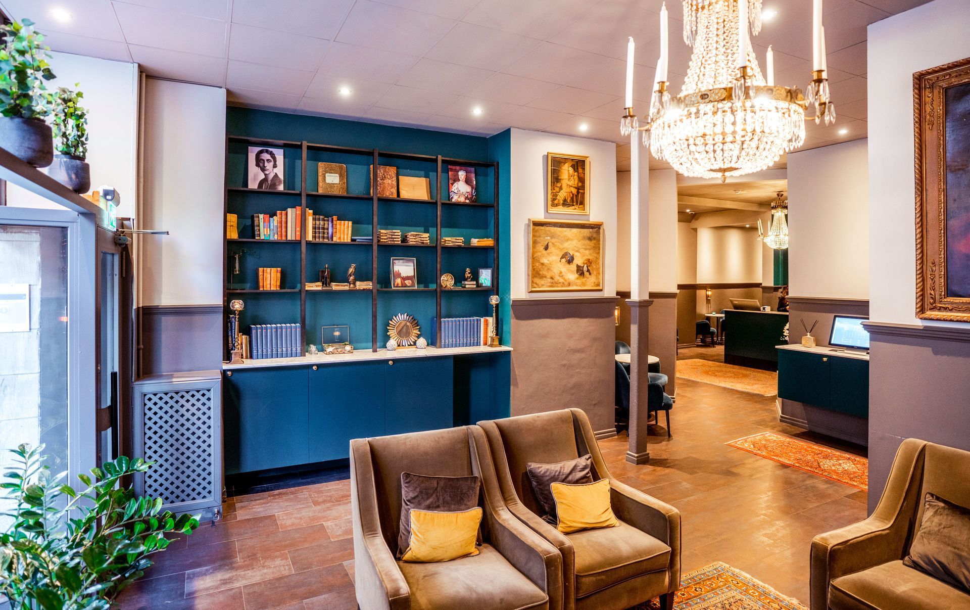 Elegant lounge with teal shelving, gold chandelier, and beige armchairs in a warmly lit interior