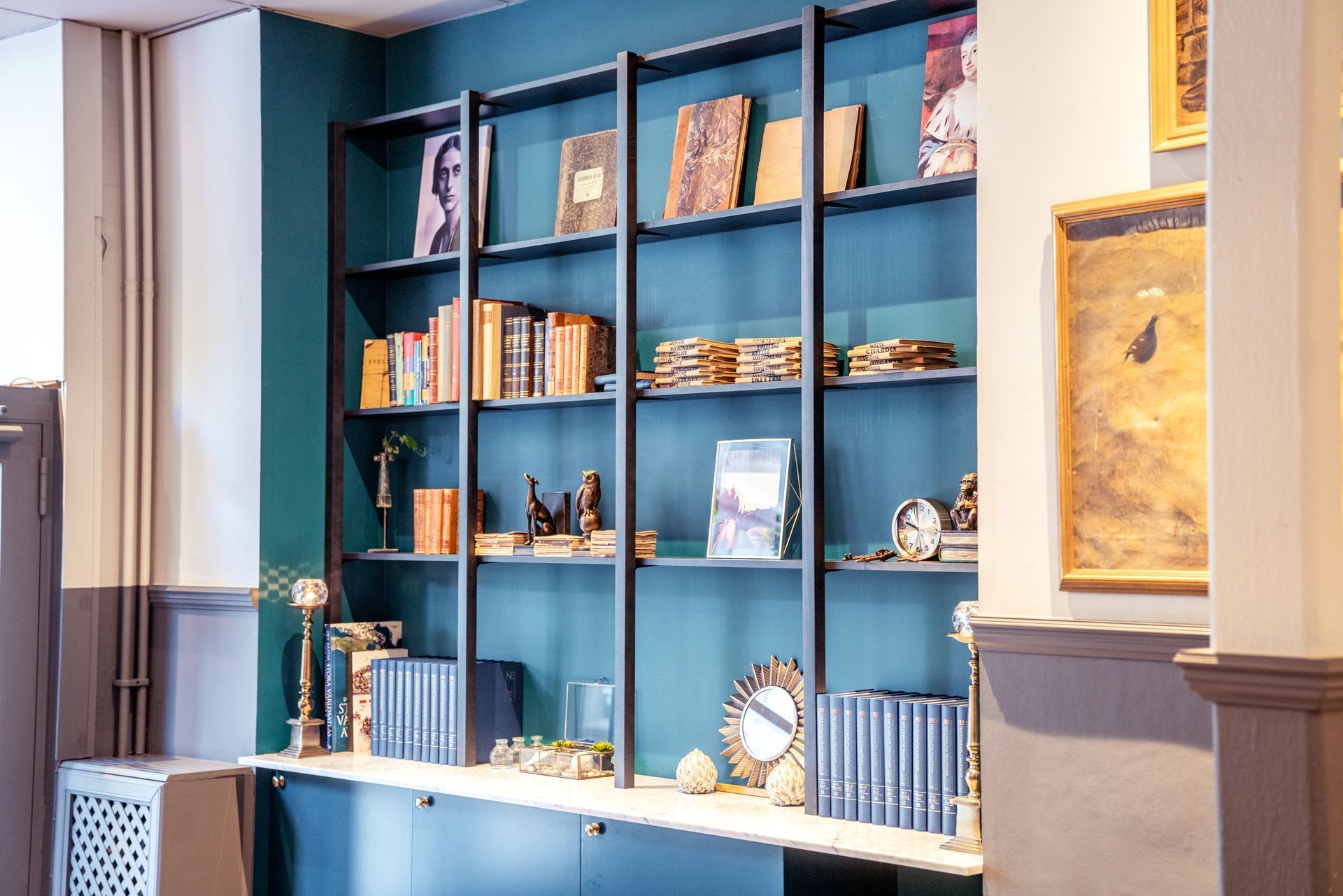 Blue built-in bookshelf displaying books, framed art, and decorative objects in a room