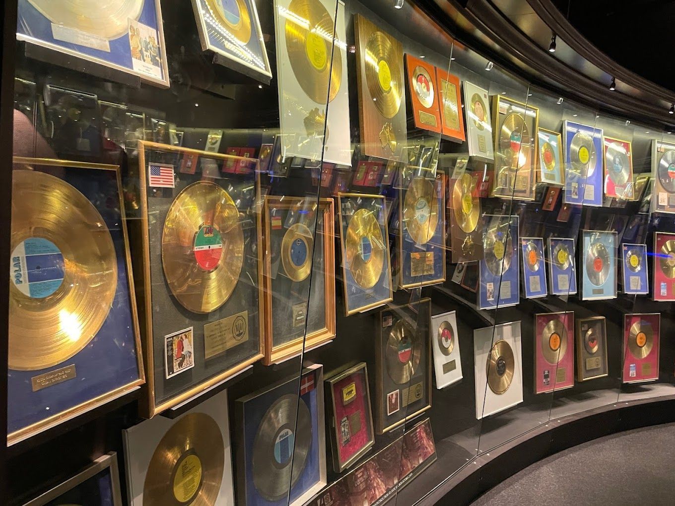 Wall of framed gold records and music awards displayed in a curved, dimly lit gallery.